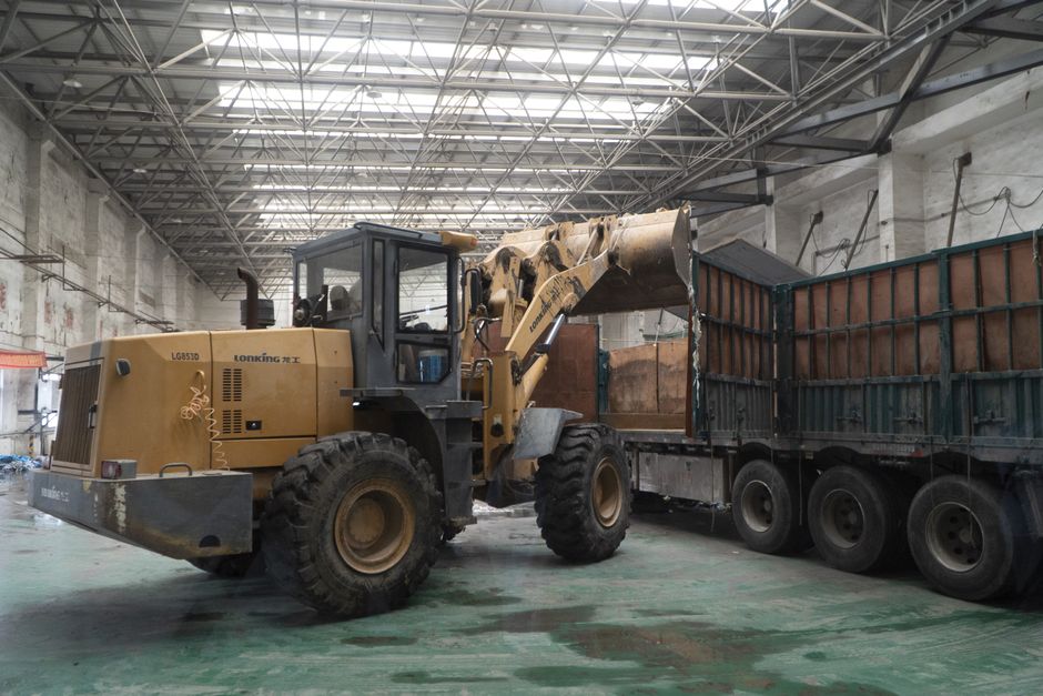 Heavy-duty loader transferring materials onto a truck inside a large warehouse.